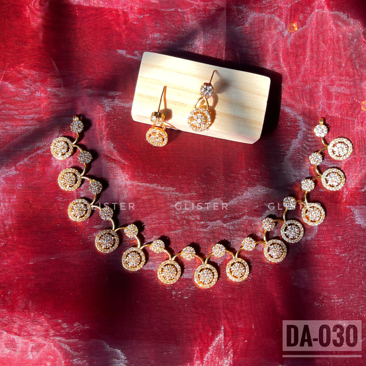 Gold-tone necklace and earrings with round clear-accent motifs laid on red fabric
