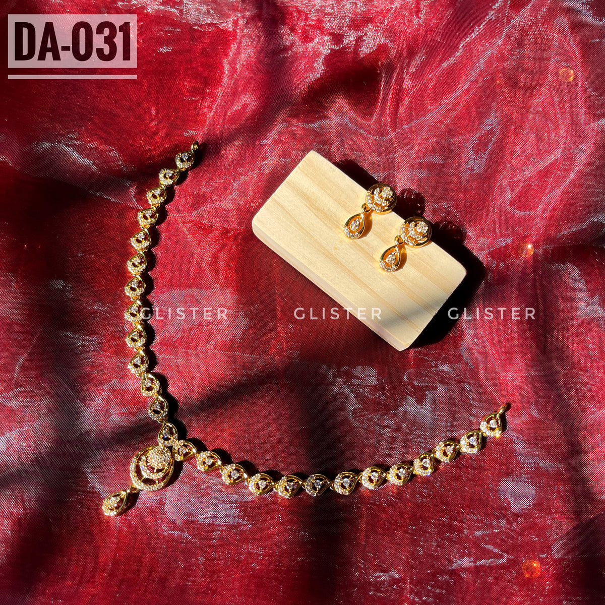 Gold-tone necklace with a teardrop pendant and matching earrings laid on red fabric