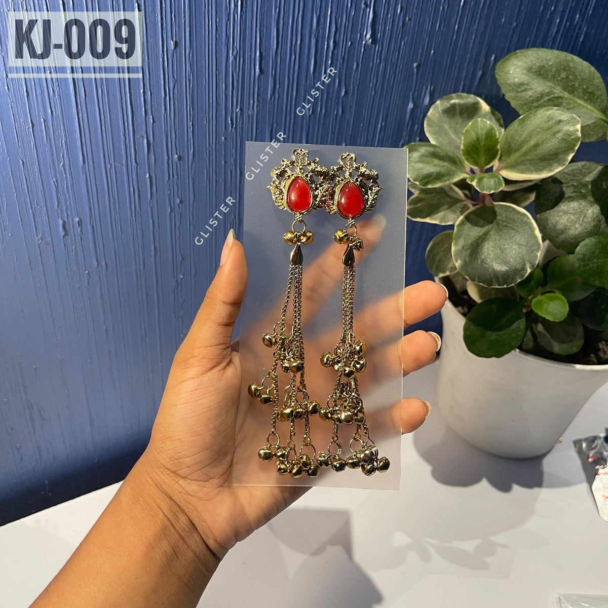 Glister KJ-009: A pair of Kashmiri-inspired long earrings with ornate tops and teardrop-shaped colored accents, hanging chains and clusters of small bell-like drops, alternate view held in hand.