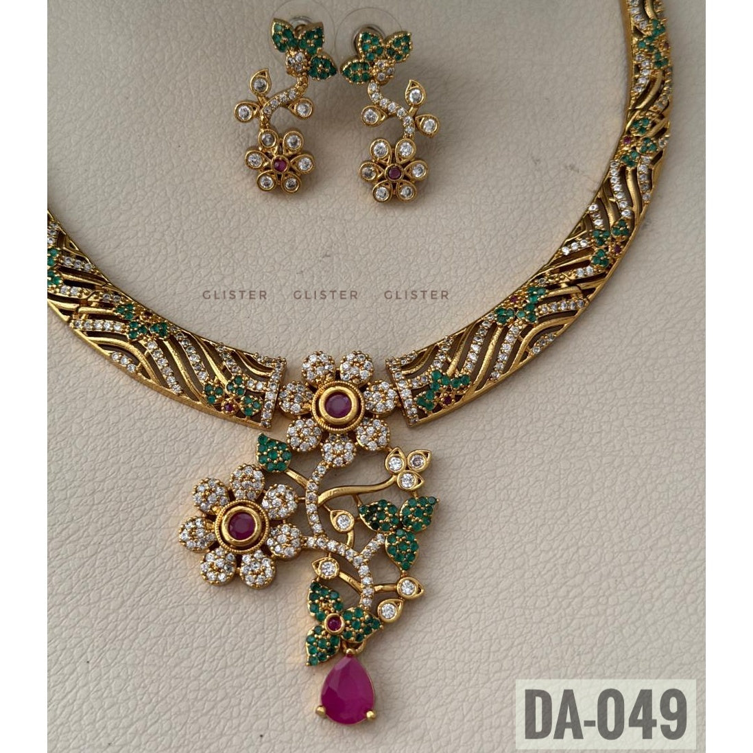 Glister DA-049: A curved patterned necklace with floral and leaf details, a pink teardrop pendant and matching floral drop earrings, alternate close-up.