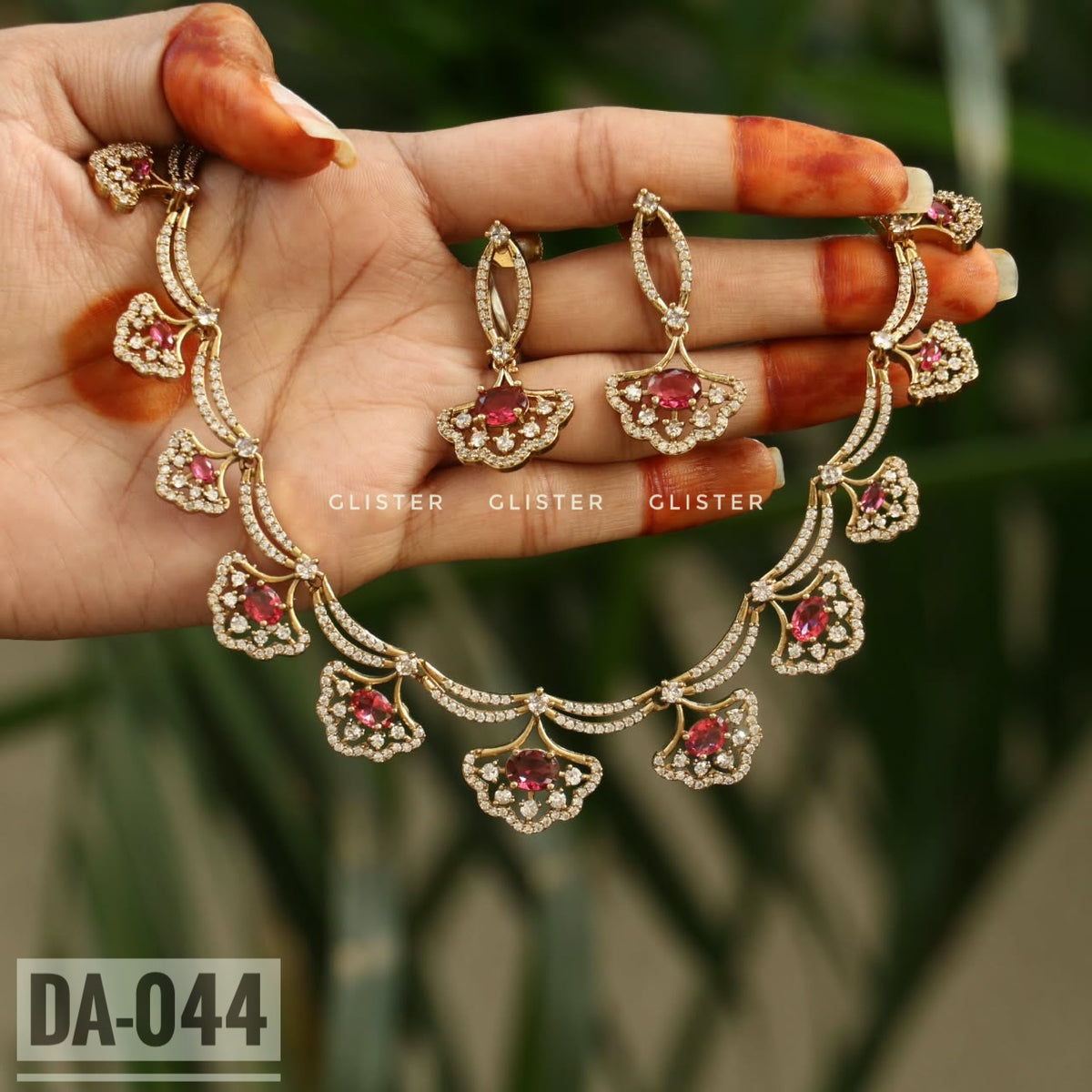 Gold-tone necklace with red floral drops and matching earrings held in a hand