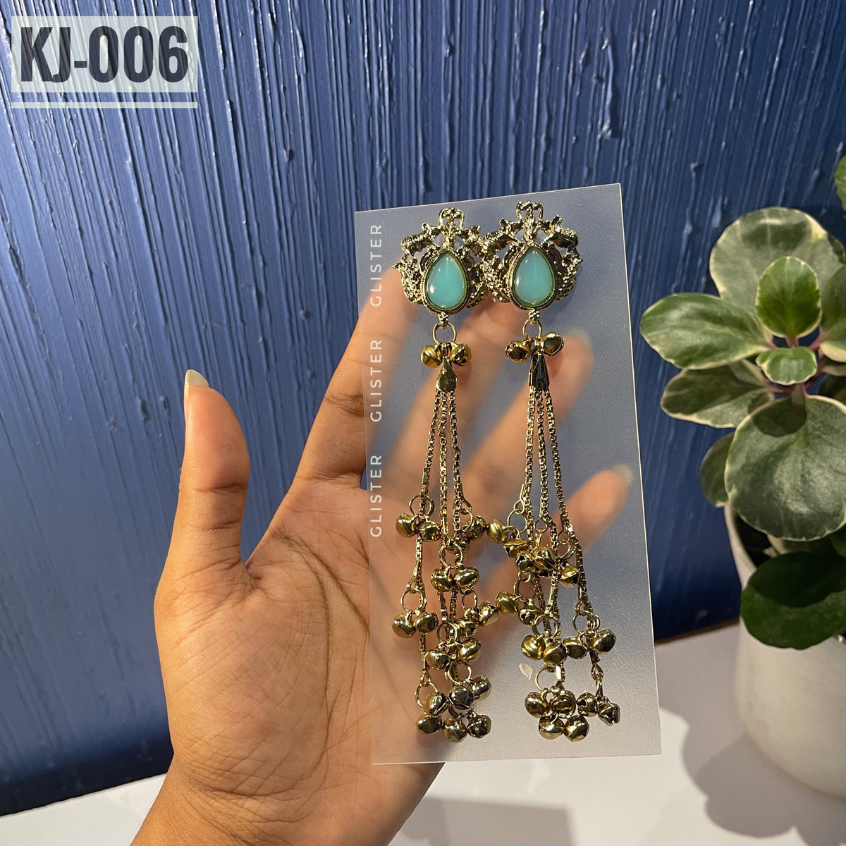 Glister KJ-006: A pair of Kashmiri-inspired long earrings with ornate tops and teardrop-shaped colored accents, hanging chains and clusters of small bell-like drops, alternate view held in hand.