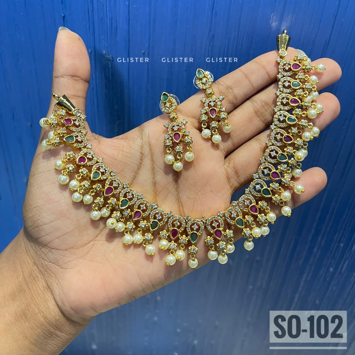 Gold-tone choker with colored accents, white bead fringe and matching earrings held in a hand