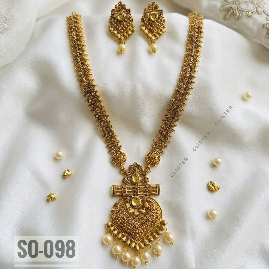 Gold-tone long necklace with a heart-shaped pendant and matching earrings on fabric