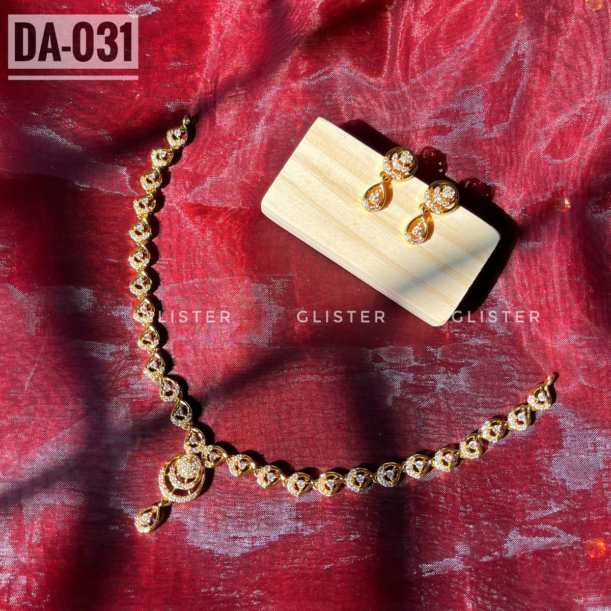 Gold-tone necklace with a teardrop pendant and matching earrings laid on red fabric