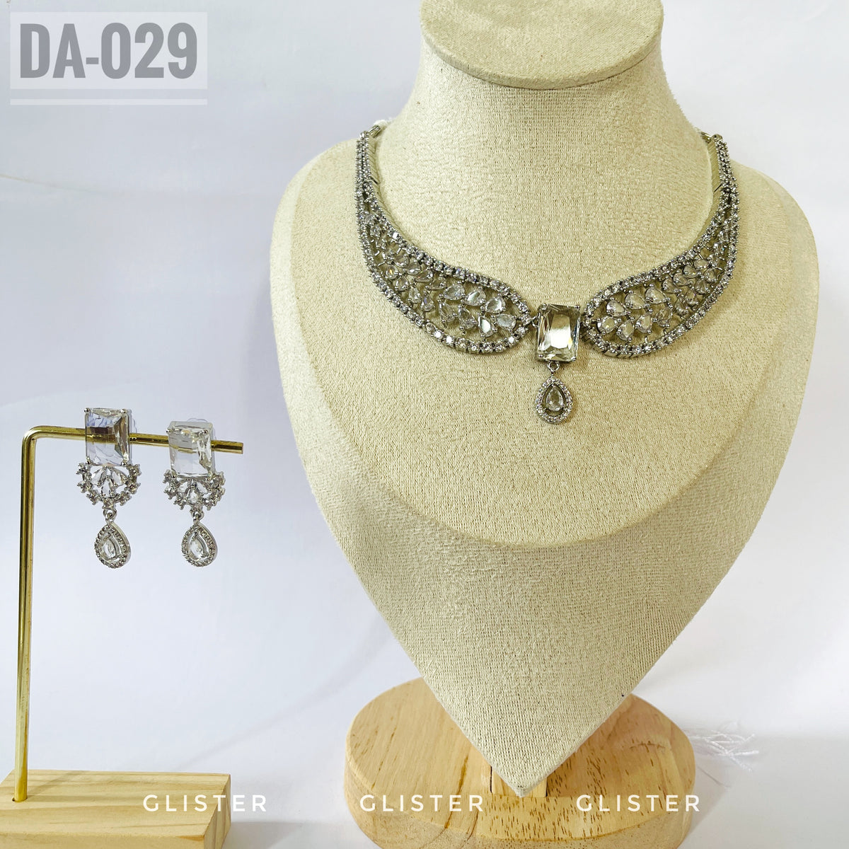 Silver-tone openwork necklace with a central drop and matching earrings on a display bust