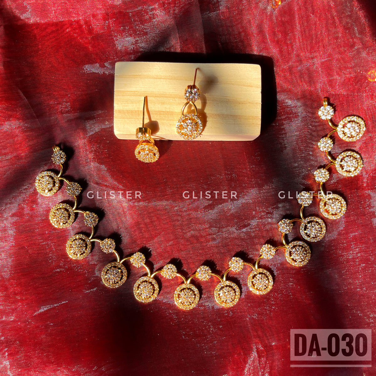 Gold-tone necklace and earrings with round clear-accent motifs laid on red fabric