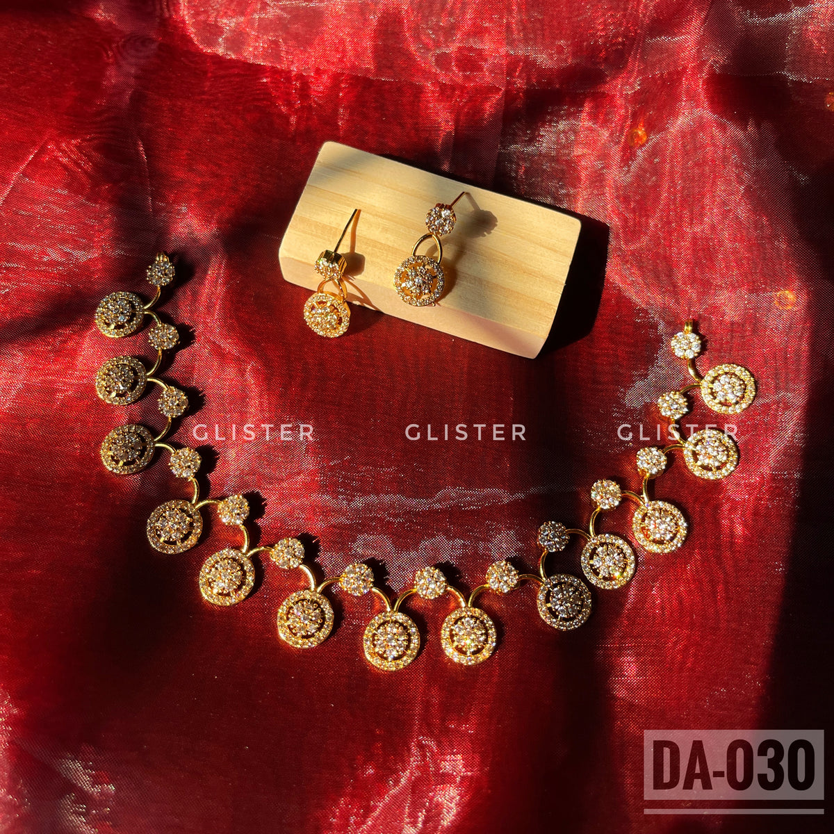 Gold-tone necklace and earrings with round clear-accent motifs laid on red fabric