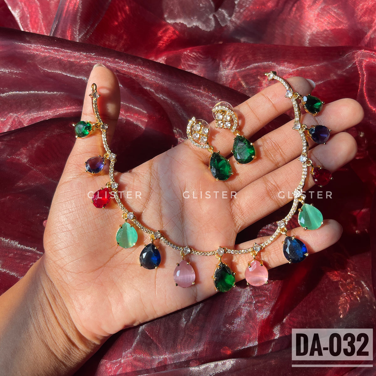 Gold-tone necklace with multicolor teardrop accents and matching green earrings held in a hand