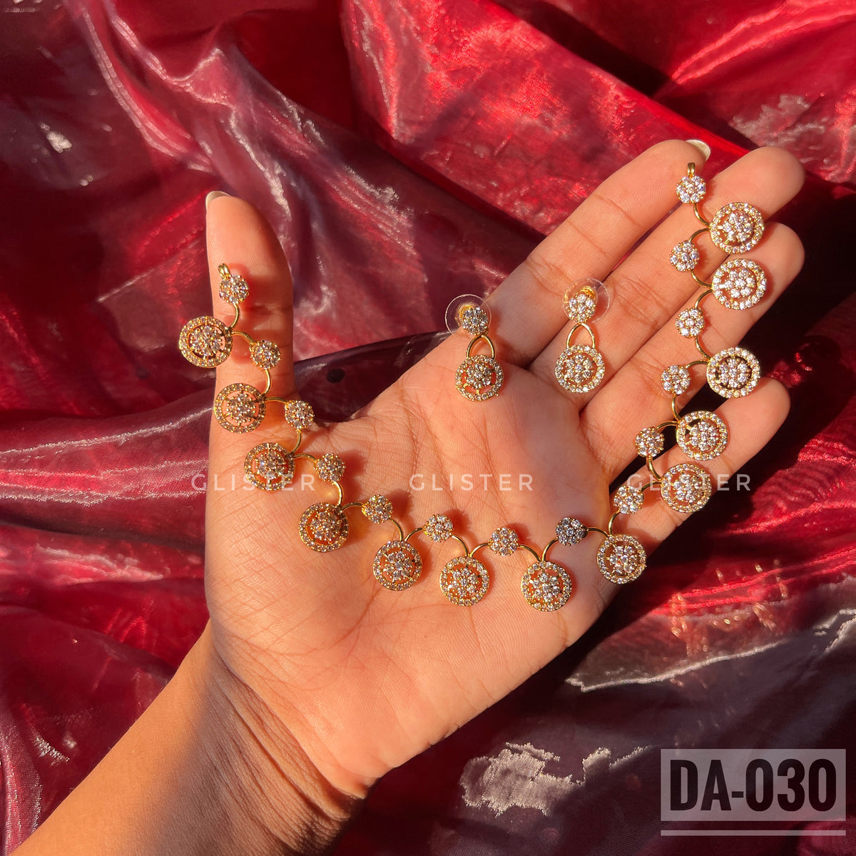 Gold-tone necklace and earrings with round clear-accent motifs held in a hand