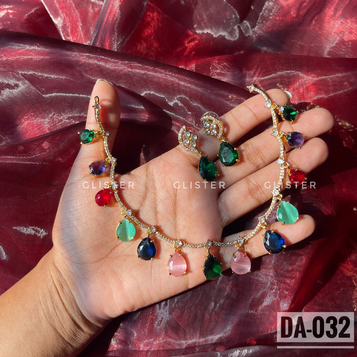 Gold-tone necklace with multicolor teardrop accents and matching green earrings held in a hand