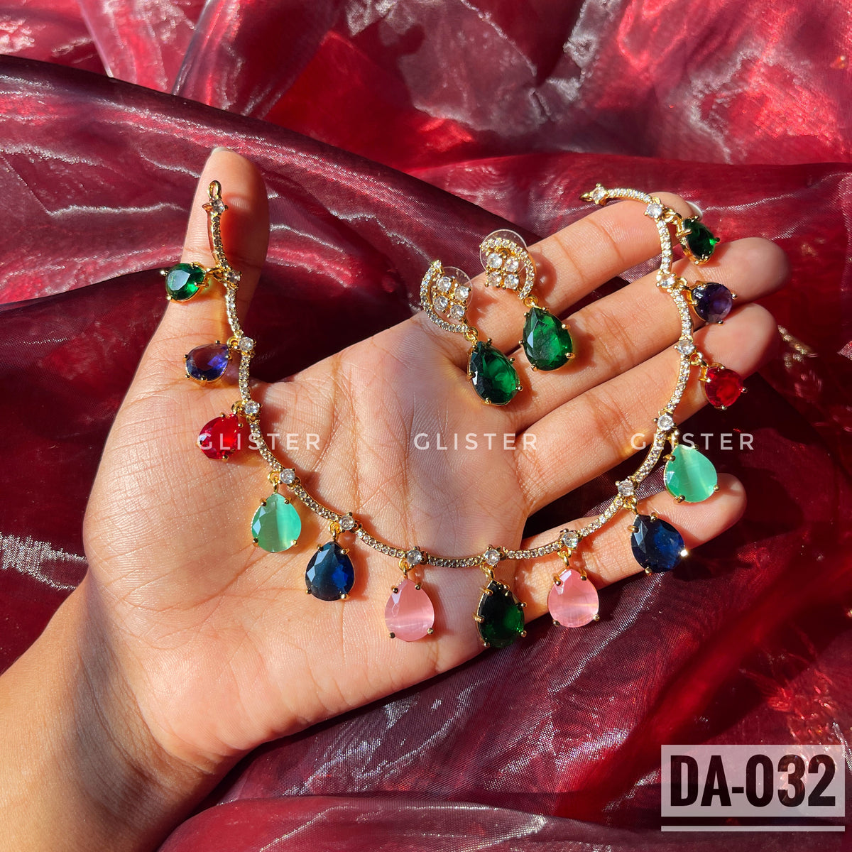 Gold-tone necklace with multicolor teardrop accents and matching green earrings held in a hand