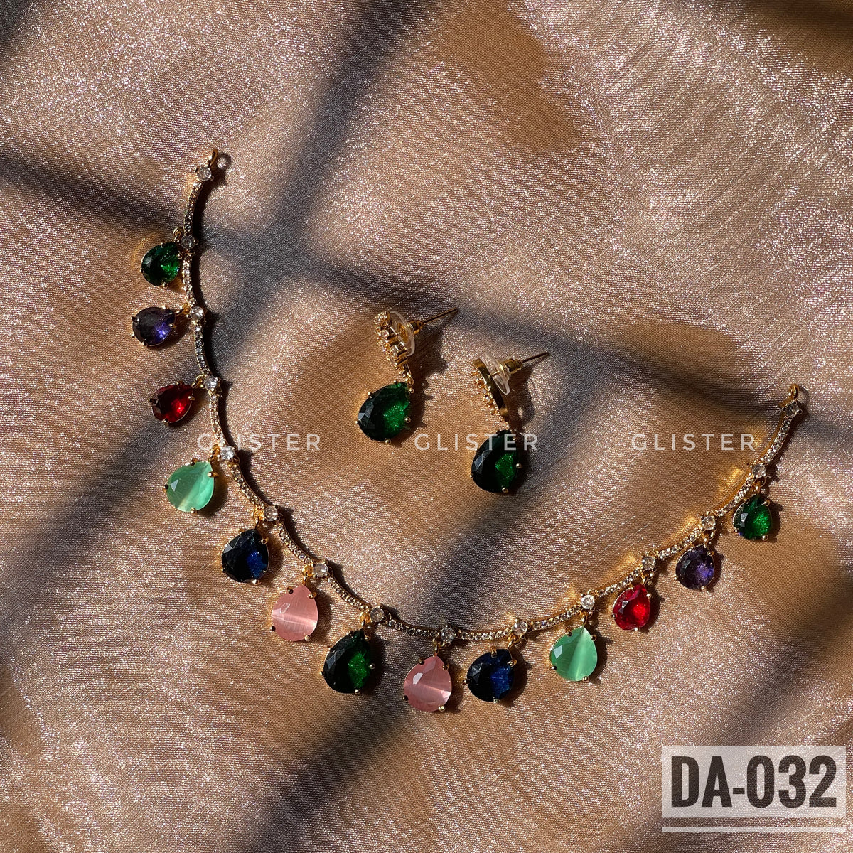 Gold-tone necklace with multicolor teardrop accents and matching green earrings laid on fabric