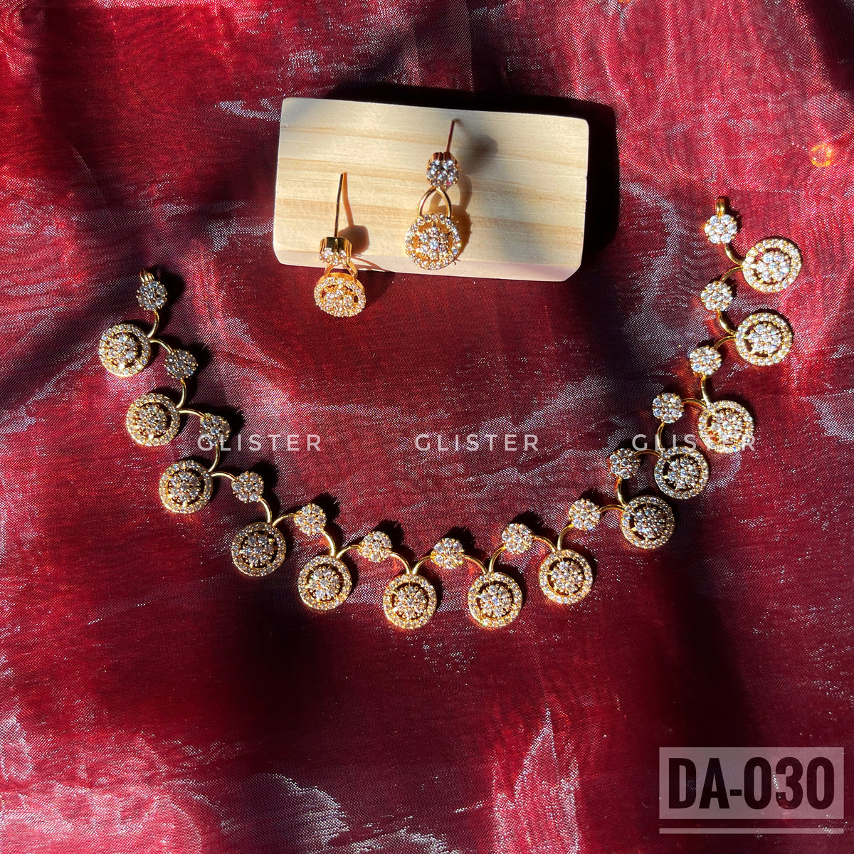 Gold-tone necklace and earrings with round clear-accent motifs laid on red fabric