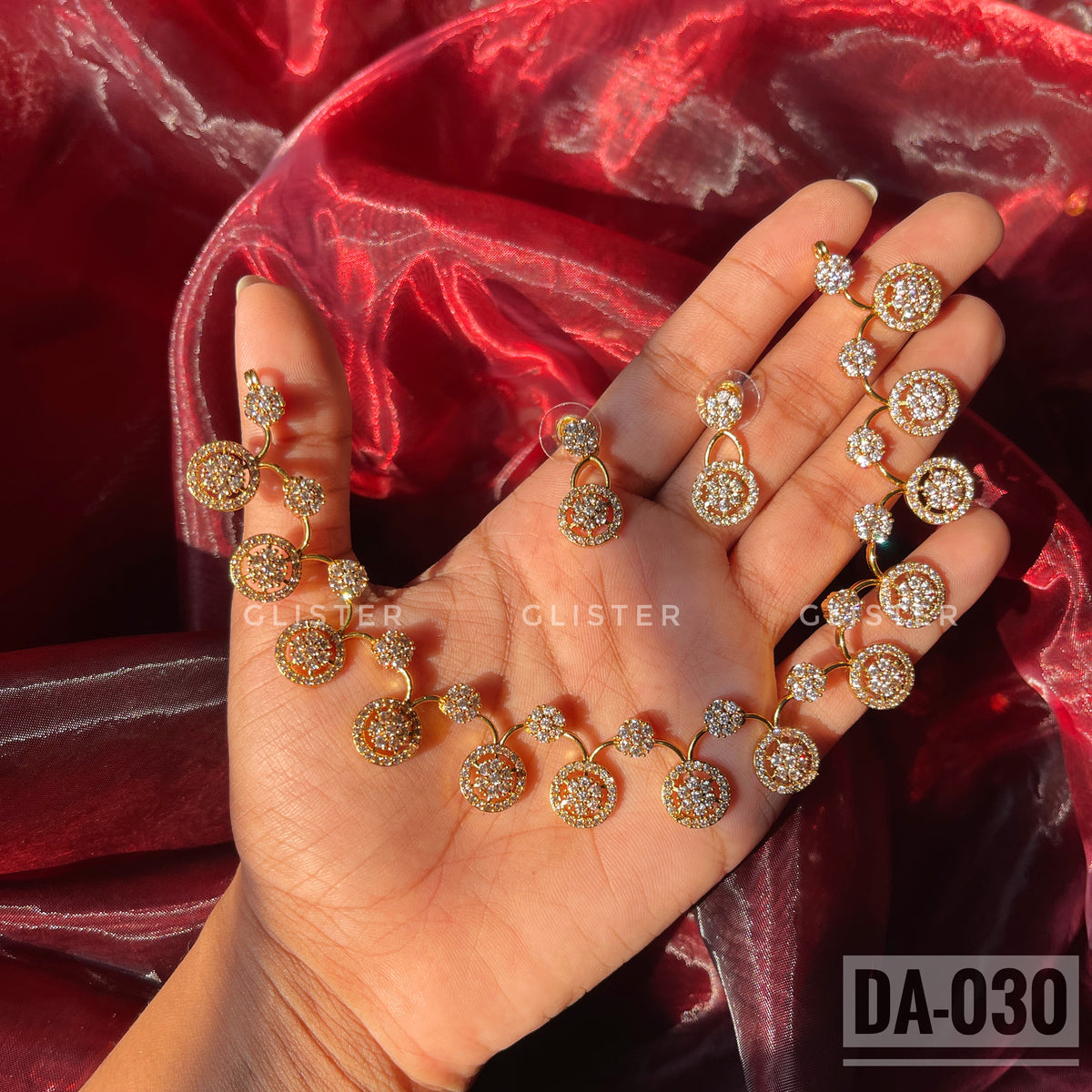 Gold-tone necklace and earrings with round clear-accent motifs held in a hand
