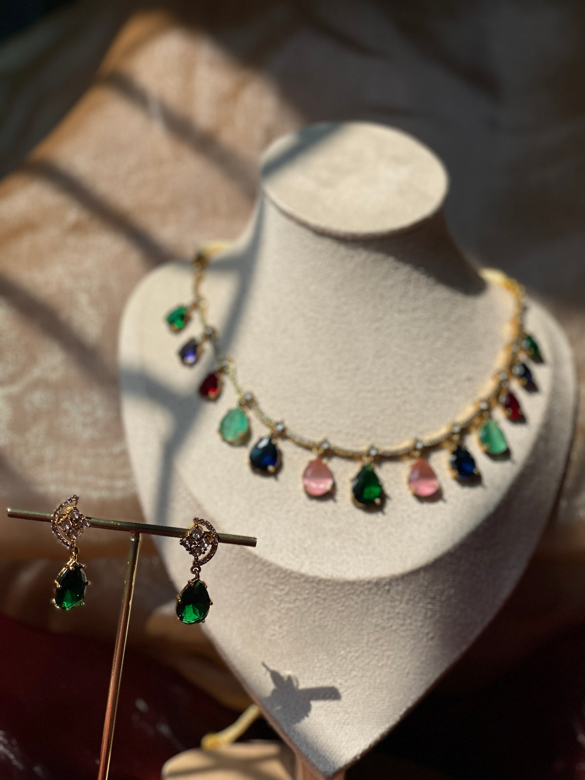 Gold-tone necklace with multicolor teardrop accents and matching green earrings on a display bust