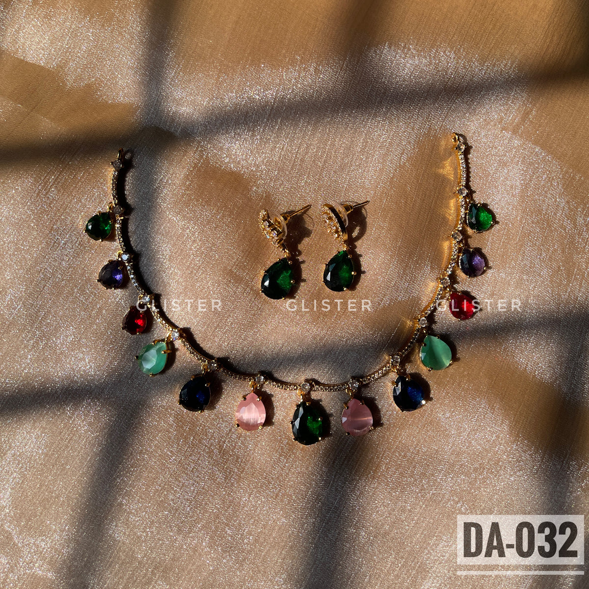 Gold-tone necklace with multicolor teardrop accents and matching green earrings laid on fabric