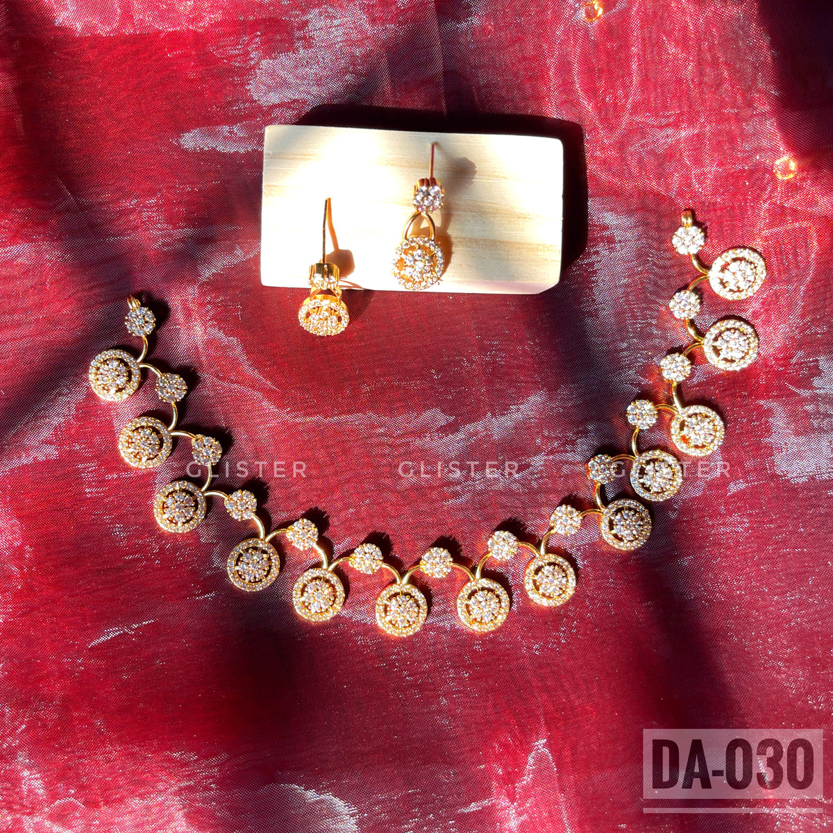 Gold-tone necklace and earrings with round clear-accent motifs laid on red fabric