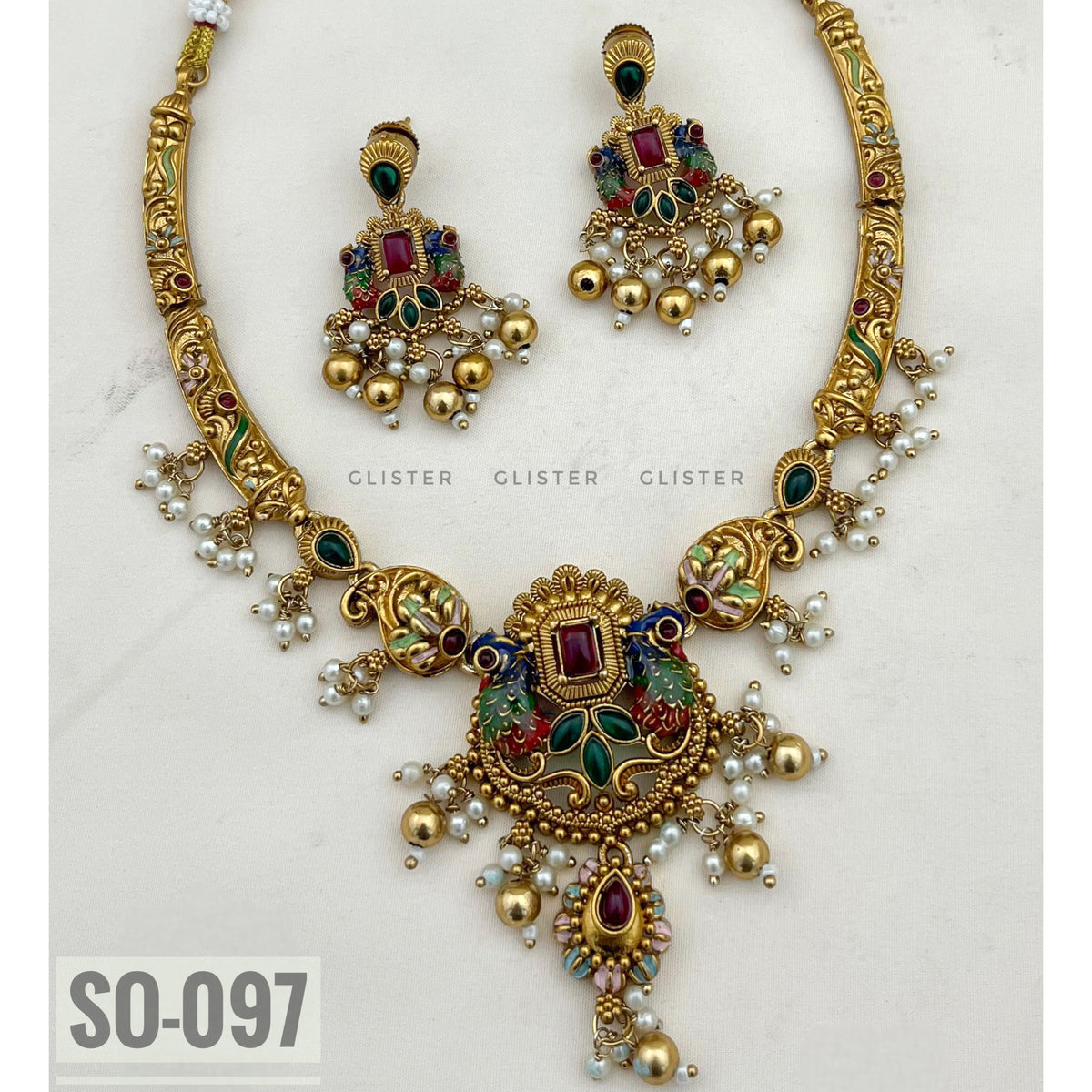 Gold-tone necklace with green and magenta accents, a decorative pendant and matching earrings on fabric