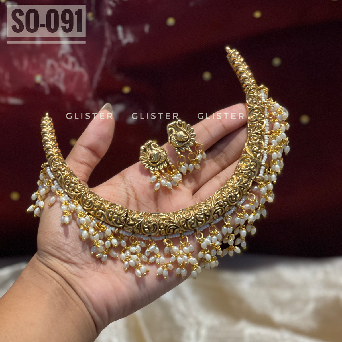 Gold-tone choker and earrings with white bead drops held in a hand