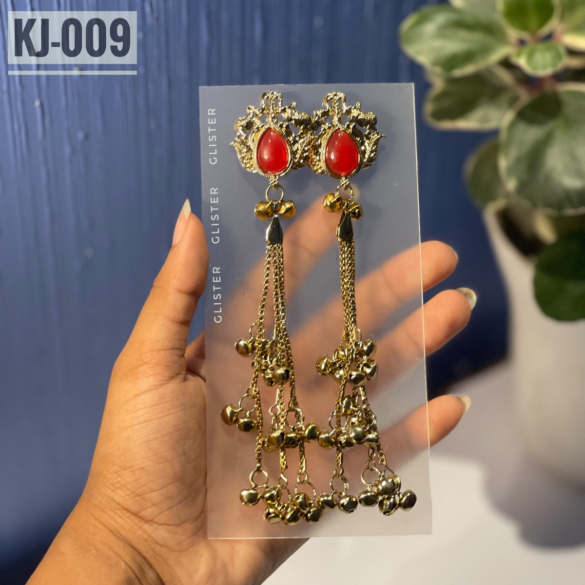 Glister KJ-009: A pair of Kashmiri-inspired long earrings with ornate tops and teardrop-shaped colored accents, hanging chains and clusters of small bell-like drops, close-up held in hand.