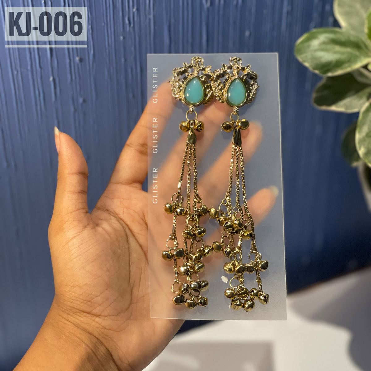 Glister KJ-006: A pair of Kashmiri-inspired long earrings with ornate tops and teardrop-shaped colored accents, hanging chains and clusters of small bell-like drops, close-up held in hand.