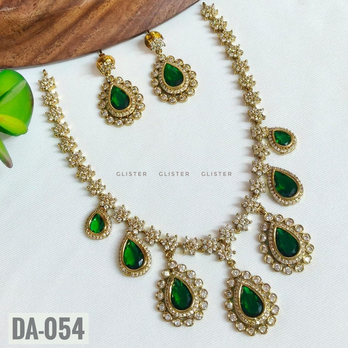 Glister DA-054: A floral-link necklace with green teardrop drops surrounded by clear decorative borders, paired with matching drop earrings.