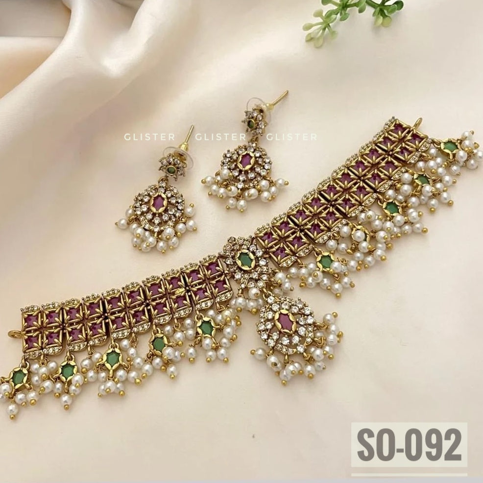 Gold-tone geometric choker with magenta accents, bead fringe, earrings and a forehead ornament on fabric