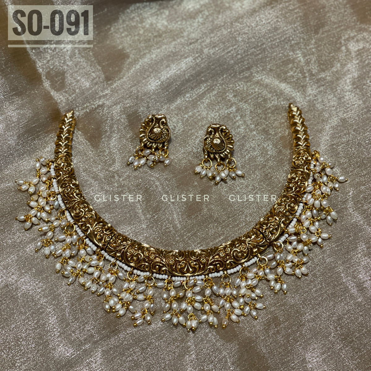 Gold-tone choker and earrings with white bead drops laid on fabric
