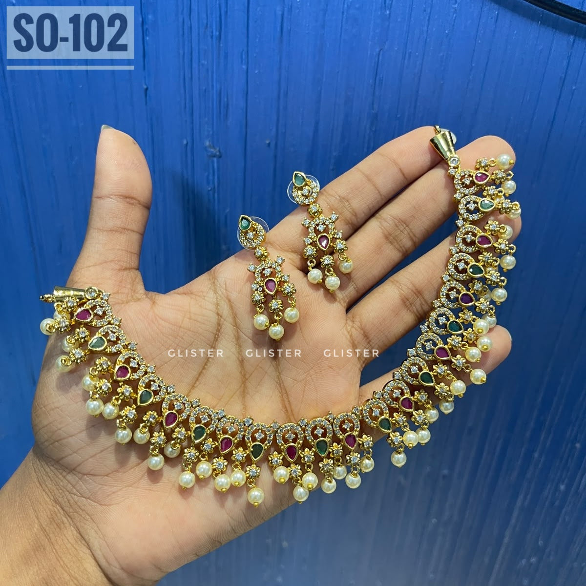 Gold-tone choker with colored accents, white bead fringe and matching earrings held in a hand