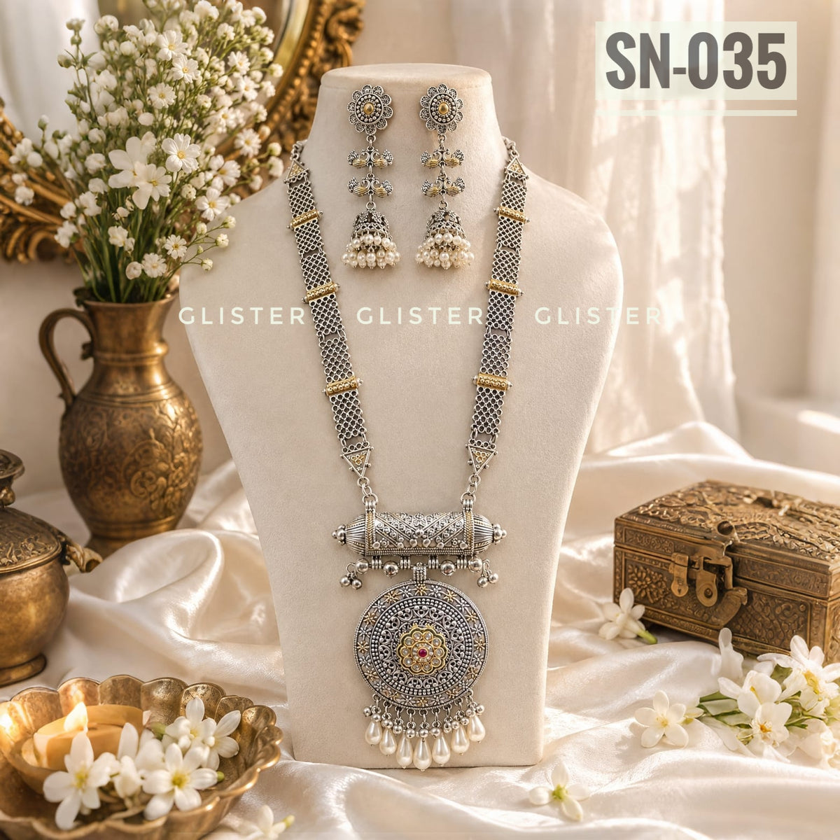 Silver-tone multi-strand necklace with a round pendant and matching earrings on a cream bust