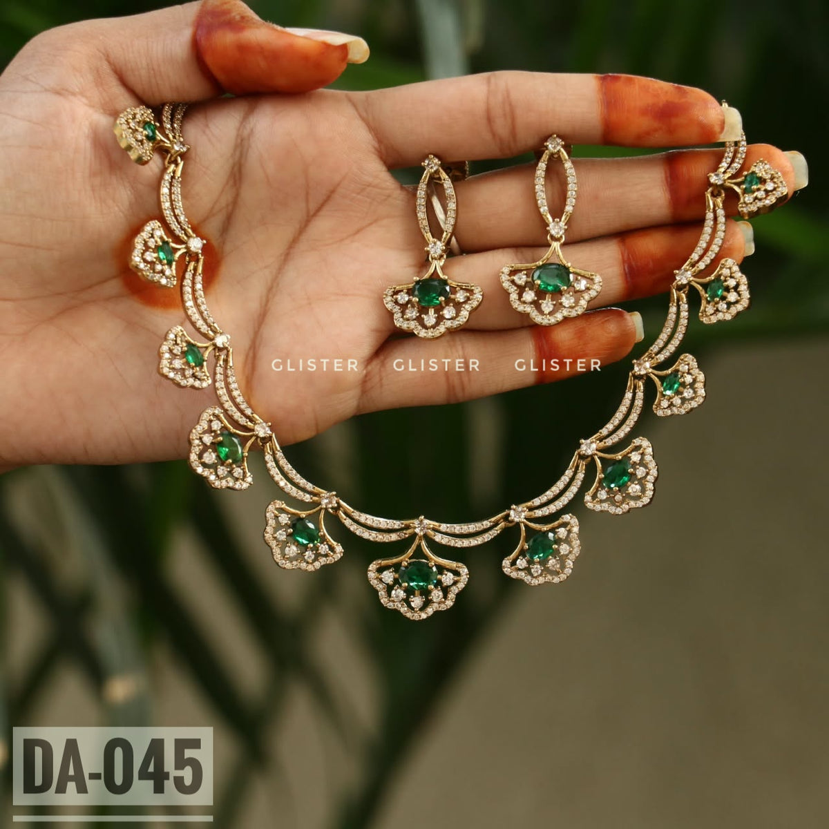 Gold-tone necklace with green floral drops and matching earrings held in a hand