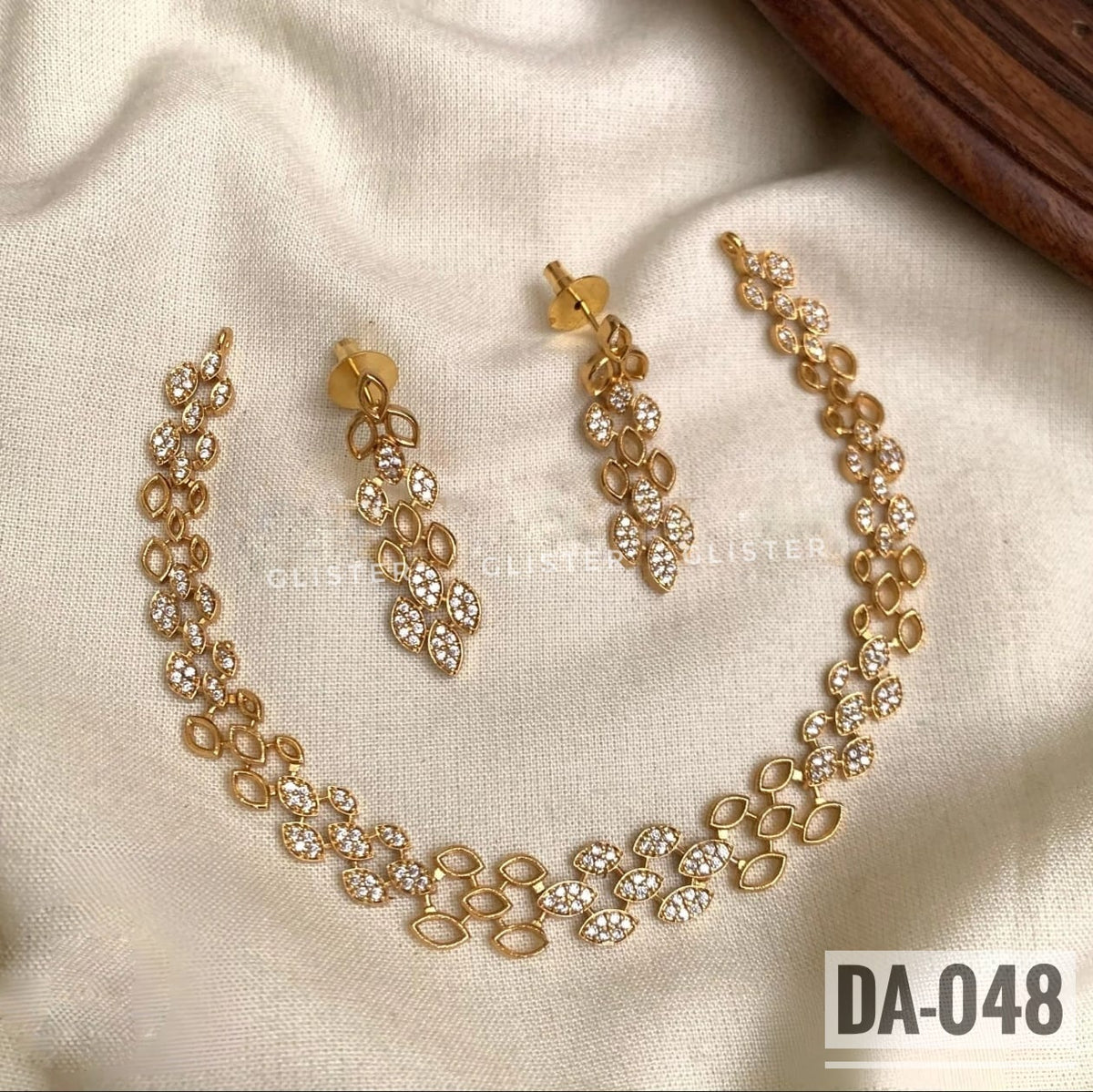 Glister DA-048: A necklace with repeating oval and floral links and clear decorative accents, paired with matching floral drop earrings.