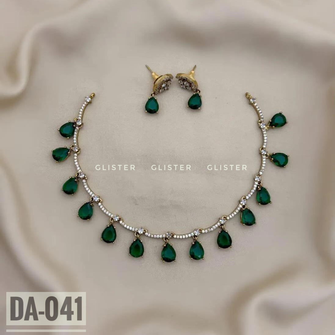 Silver-tone necklace with green teardrop accents and matching earrings on pale fabric