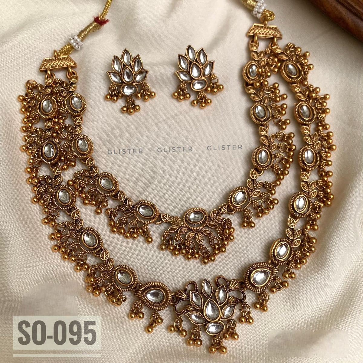 Gold-tone layered necklace design with floral motifs and matching earrings on fabric
