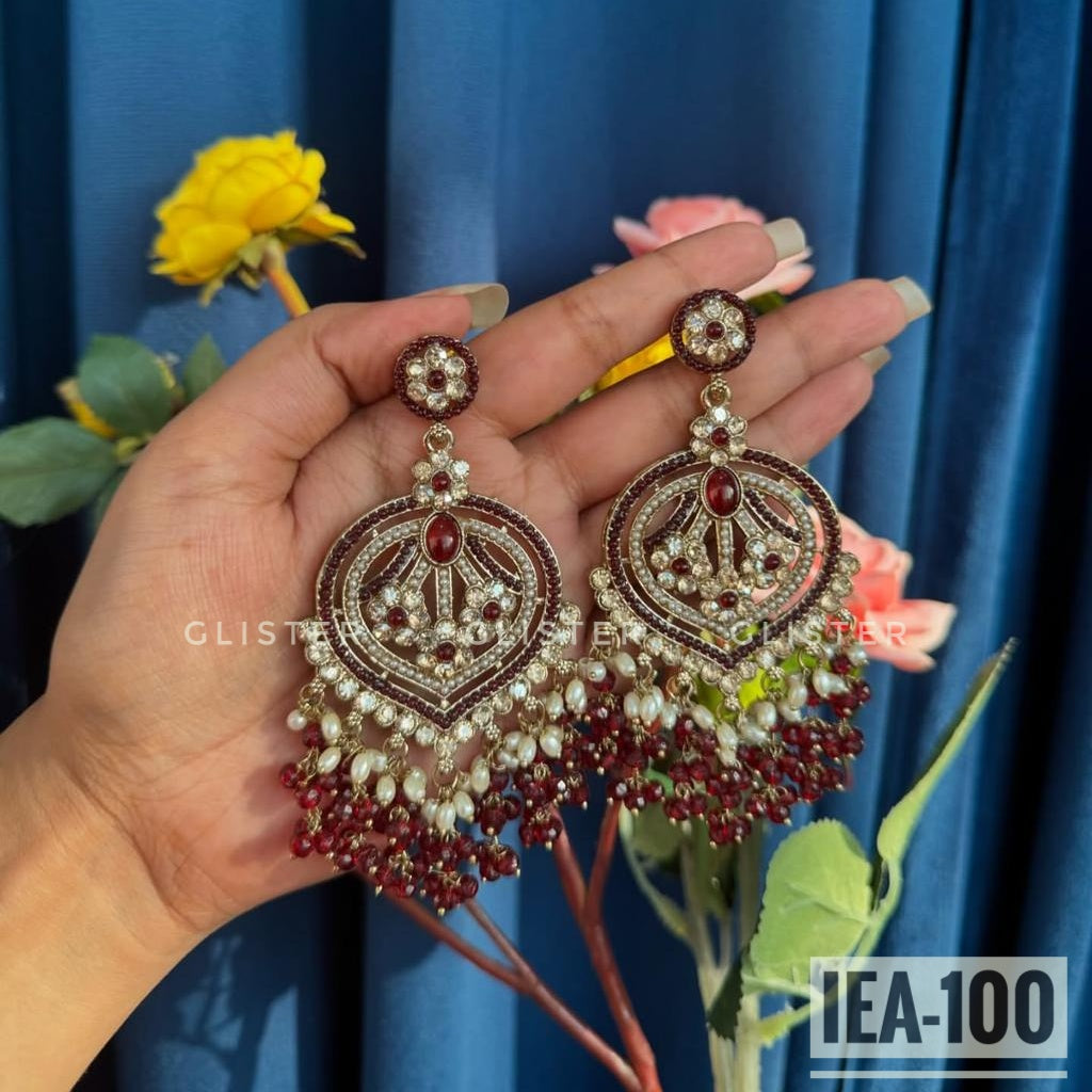 Maroon and silver-tone round earrings with a beaded fringe, held in a hand