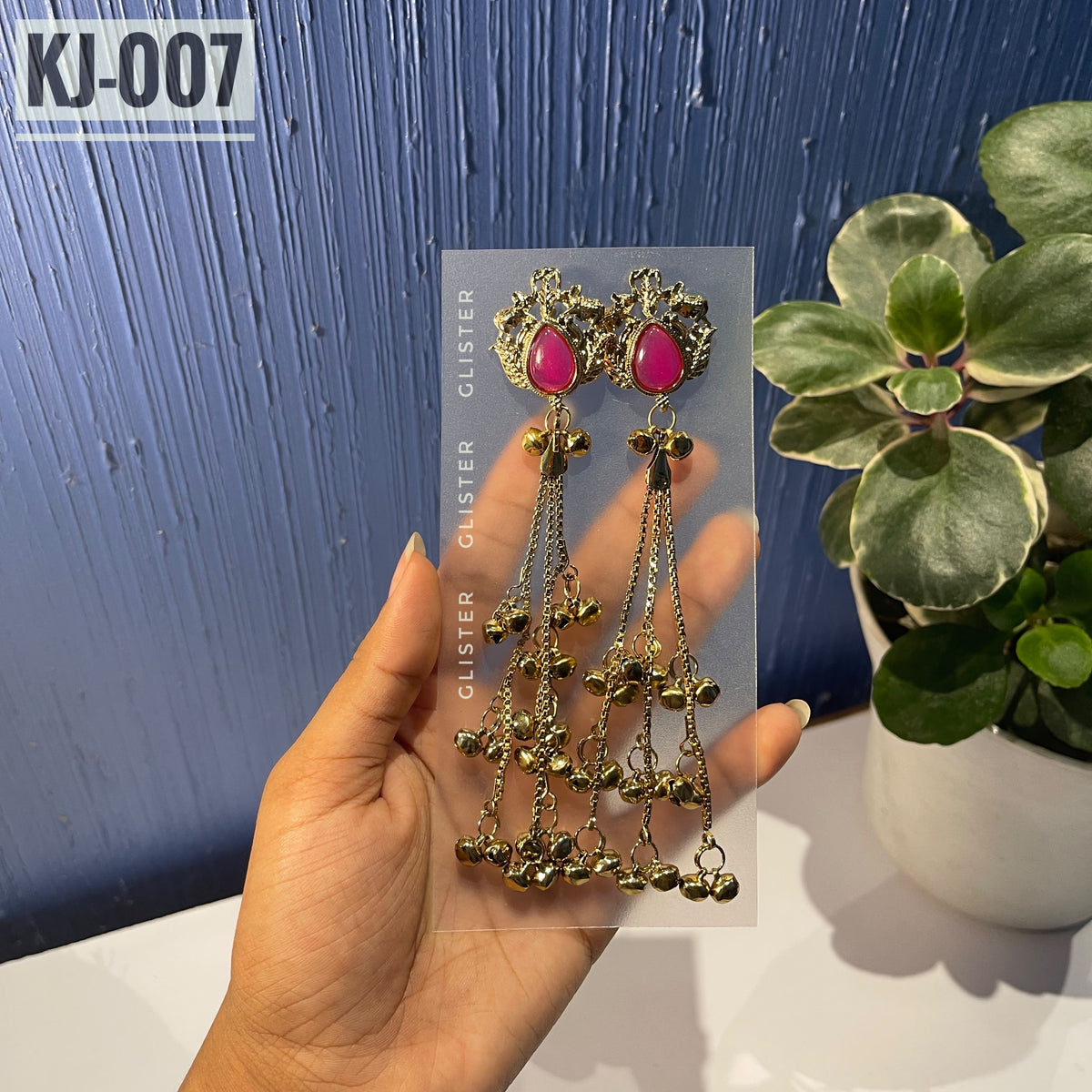 Glister KJ-007: A pair of Kashmiri-inspired long earrings with ornate tops and teardrop-shaped colored accents, hanging chains and clusters of small bell-like drops, alternate view held in hand.