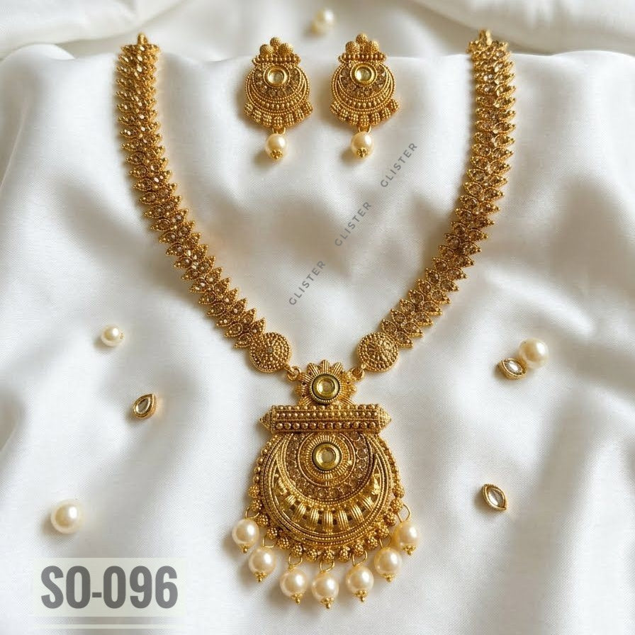 Gold-tone long necklace with a rounded pendant, white bead drops and matching earrings on fabric