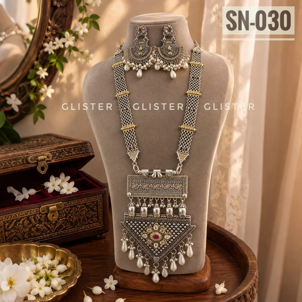 Silver-tone multi-strand necklace with a triangular pendant and matching earrings on a cream bust