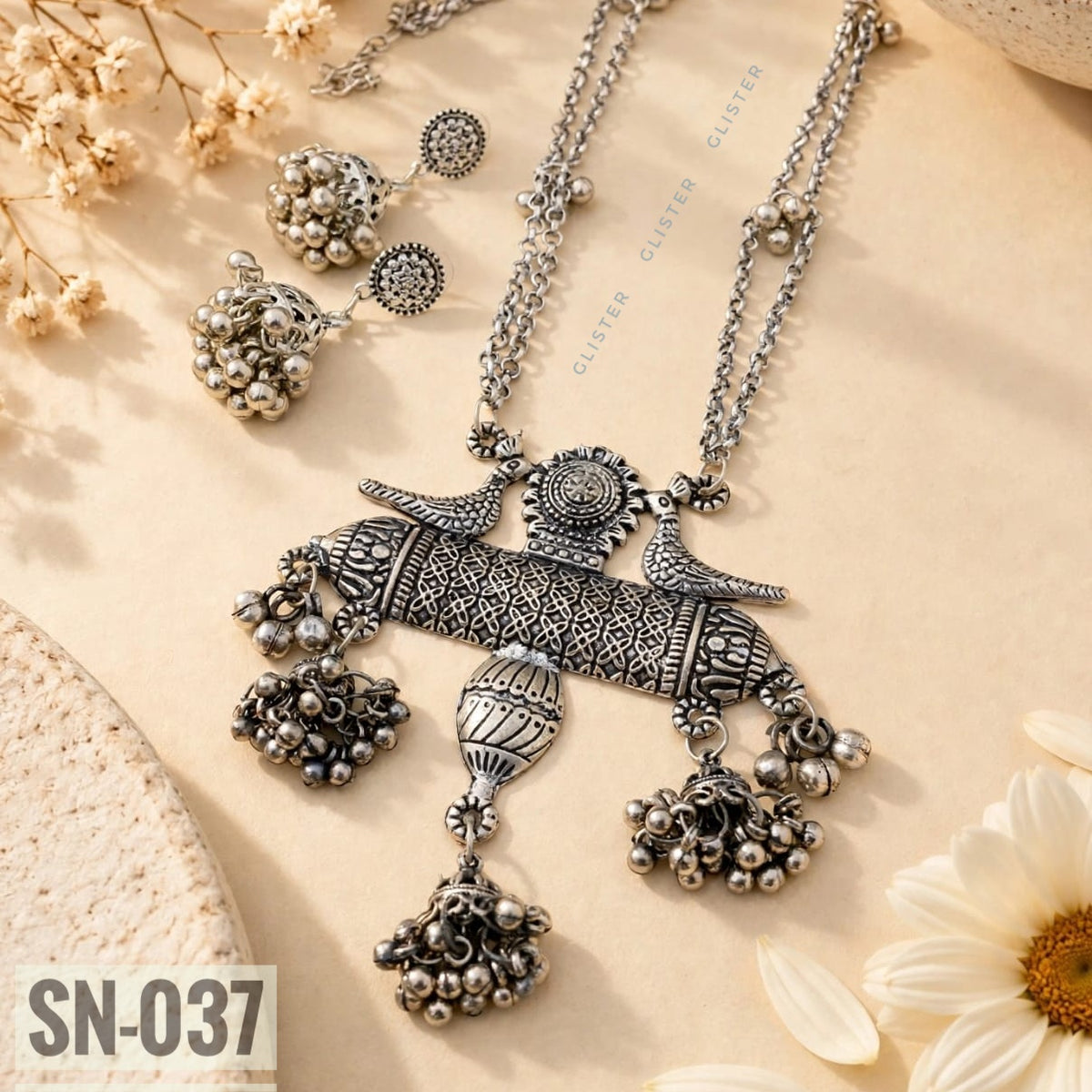 Glister SN-037: A long necklace with twin peacock motifs, a patterned bar pendant and three bell-shaped drops, paired with matching jhumka earrings.