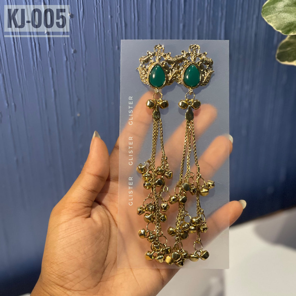Glister KJ-005: A pair of Kashmiri-inspired long earrings with ornate tops and teardrop-shaped colored accents, hanging chains and clusters of small bell-like drops, alternate view held in hand.