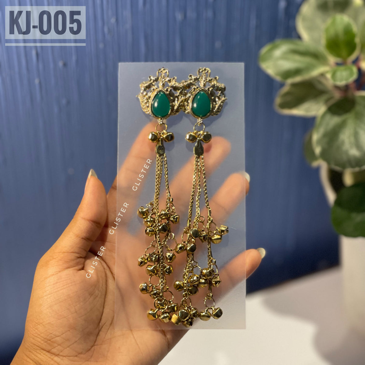 Glister KJ-005: A pair of Kashmiri-inspired long earrings with ornate tops and teardrop-shaped colored accents, hanging chains and clusters of small bell-like drops, close-up held in hand.