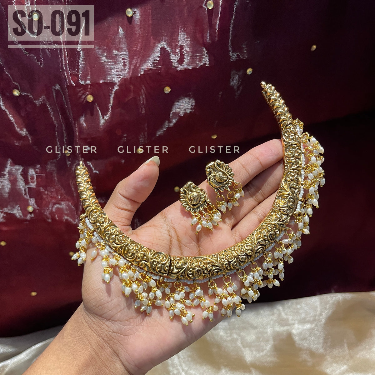 Gold-tone choker and earrings with white bead drops held in a hand