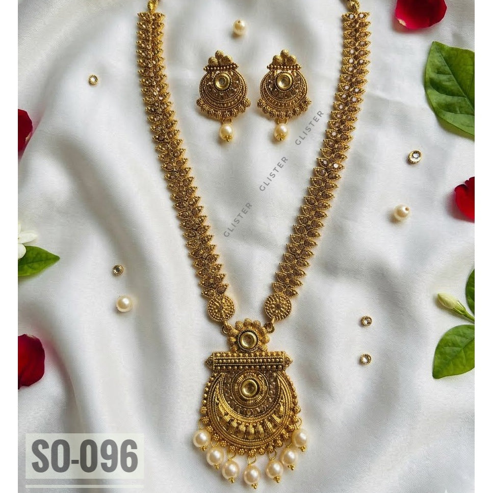 Gold-tone long necklace with a rounded pendant, white bead drops and matching earrings on fabric
