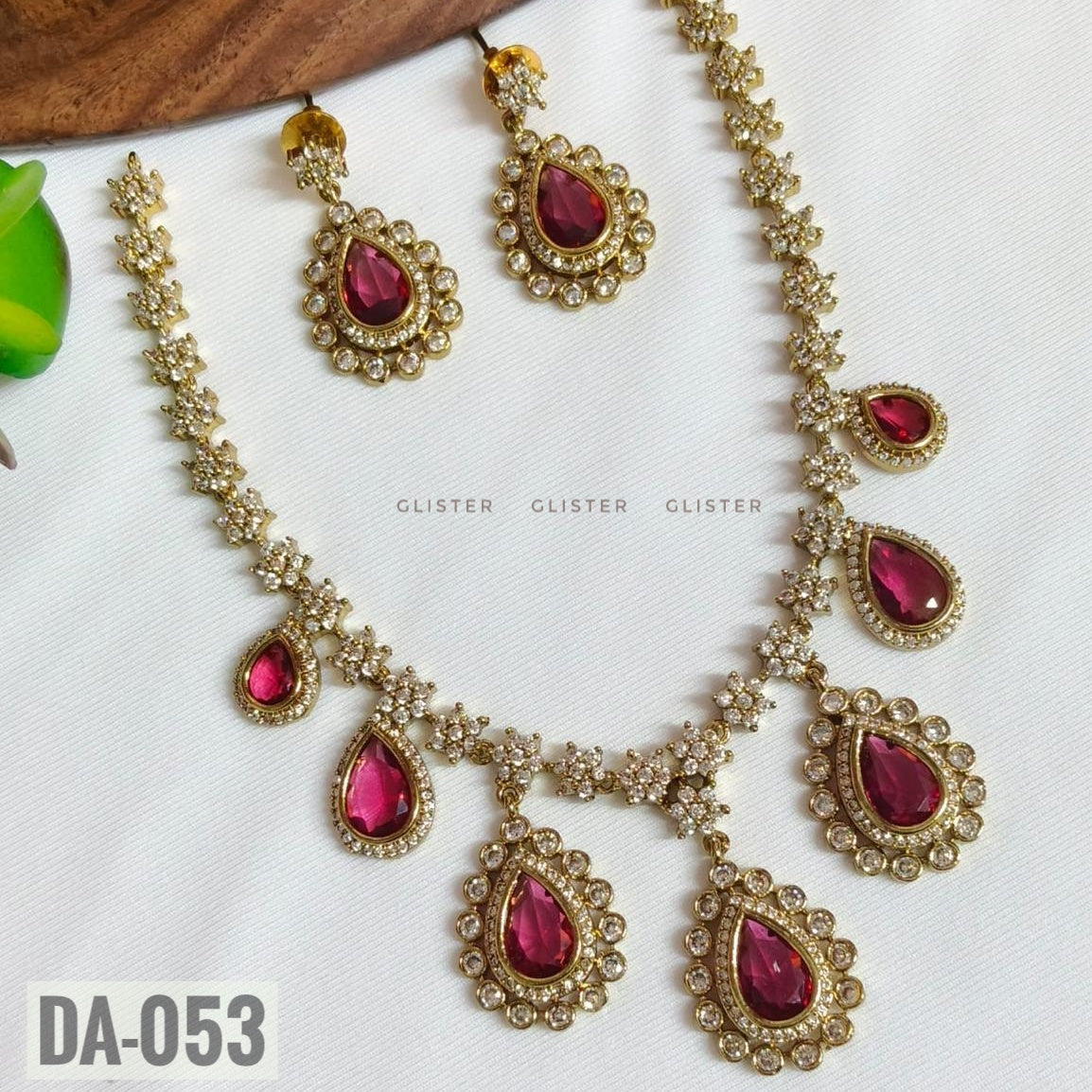 Glister DA-053: A floral-link necklace with pink teardrop drops surrounded by clear decorative borders, paired with matching drop earrings.